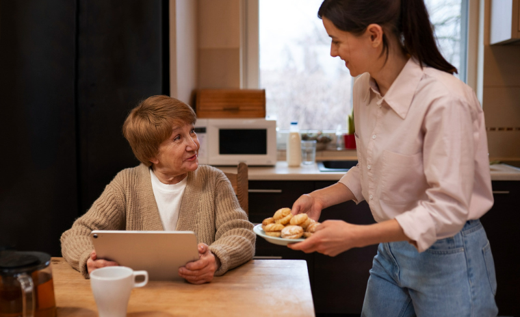 Family caregiver providing meal preparation and feeding assistance for seniors, serving fresh food to an elderly woman at home kitchen table