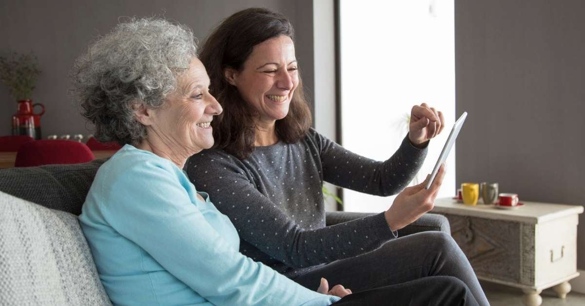 Senior woman smiling with a caregiver at home while reviewing care information on a tablet, highlighting common myths about home care and trusted in-home support in Ohio.